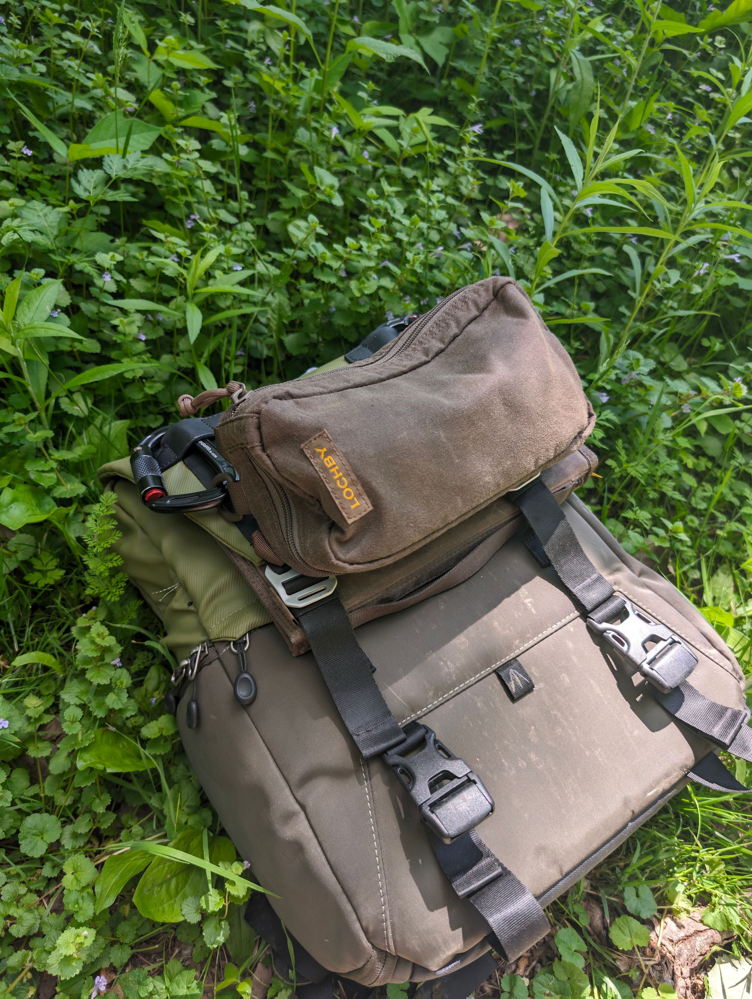 Brown and tan backpack with multiple compartments resting against green foliage.