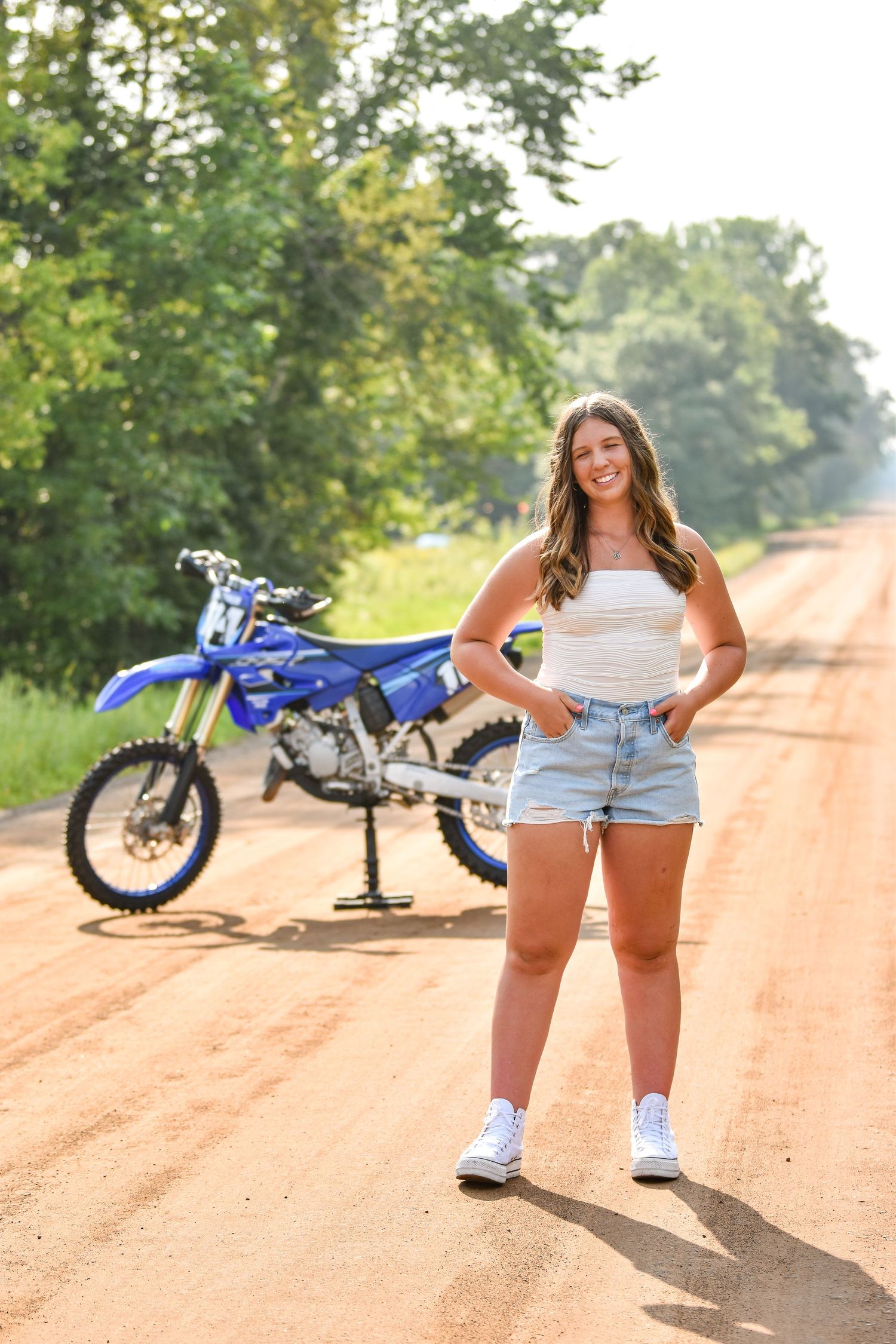 Blue dirt bike parked on a dusty red clay road with trees in the background on a sunny day.