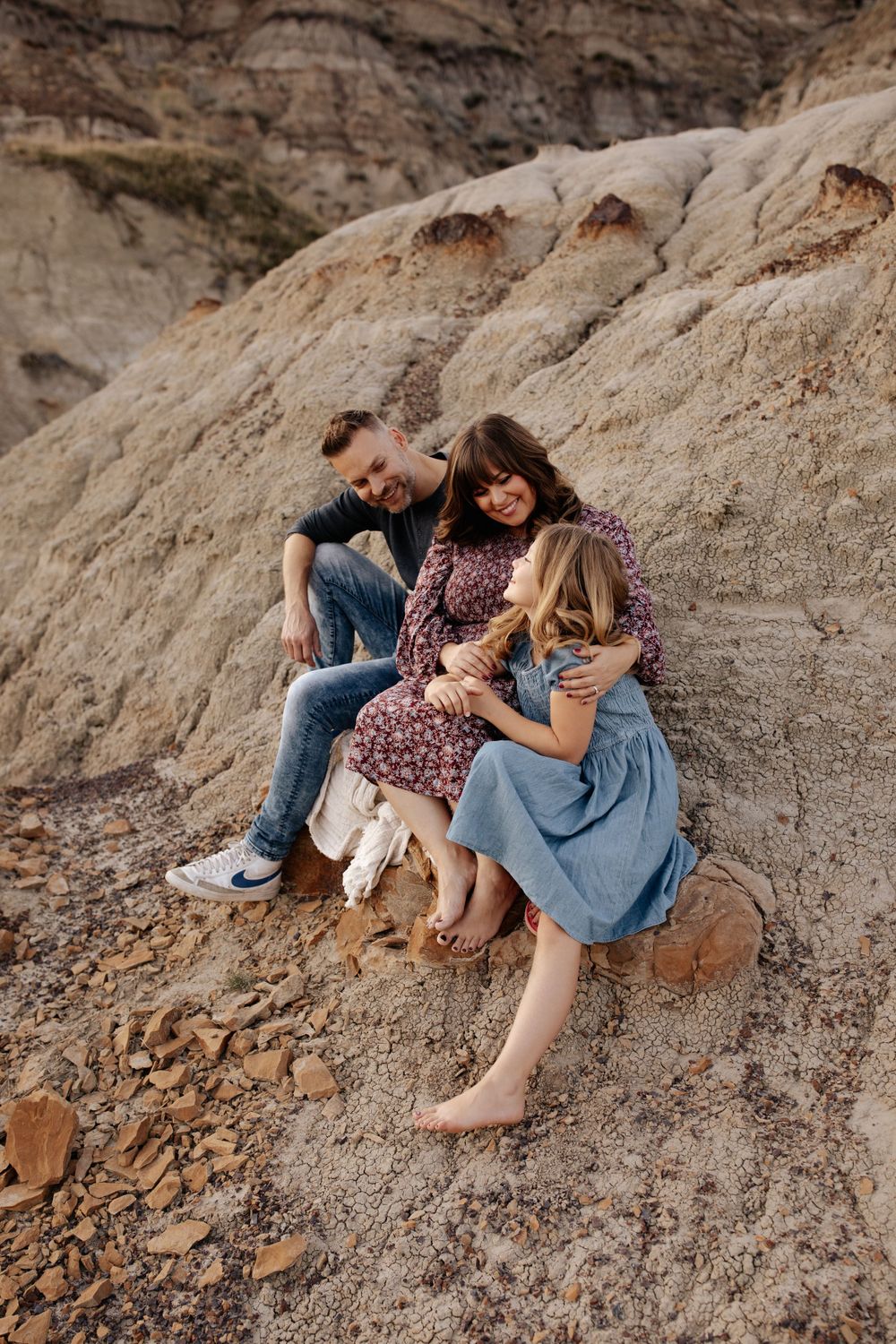 A couple shares an intimate moment while sitting on rocky terrain at sunset.