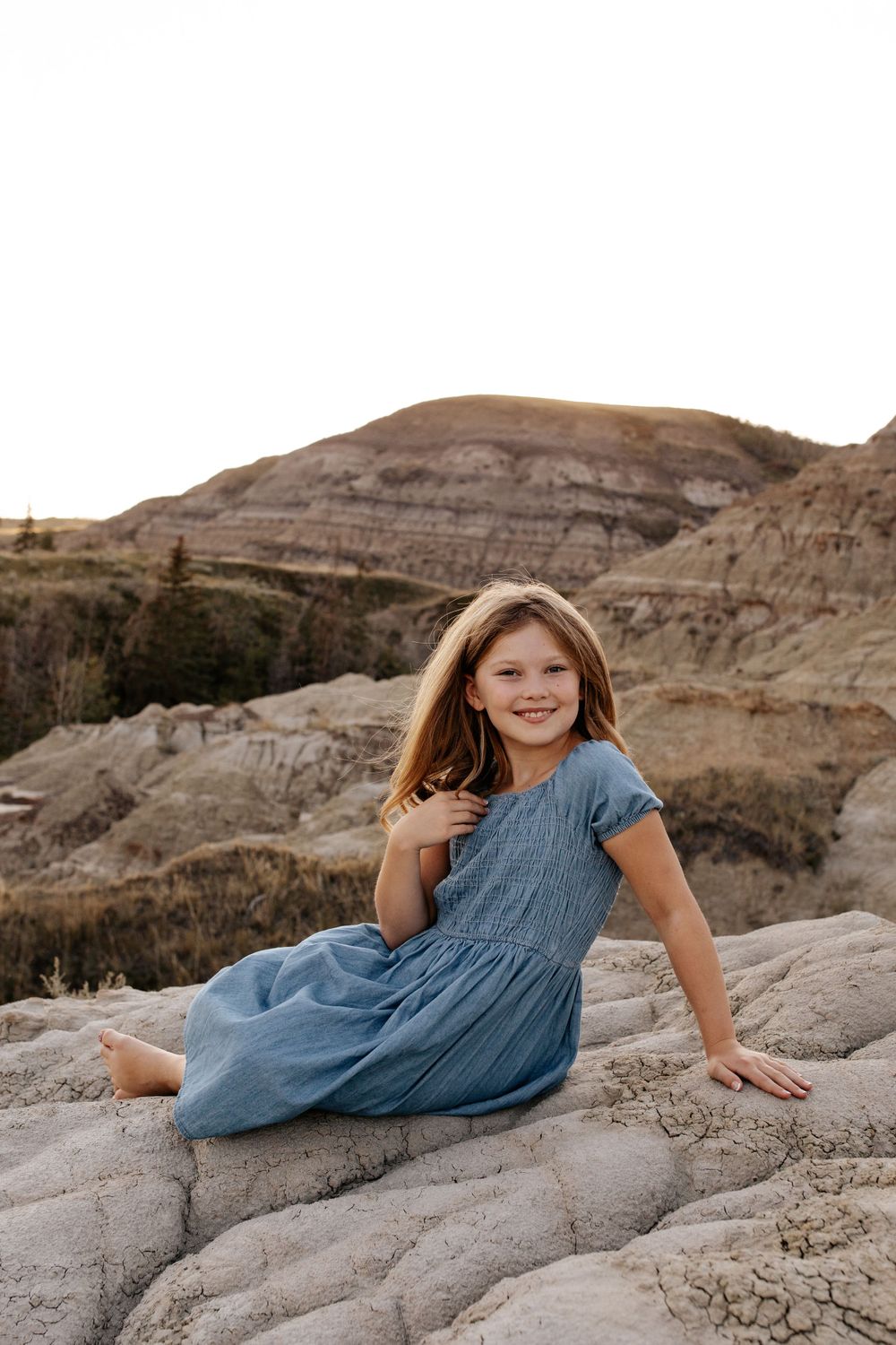 A young person in a blue dress lies playfully on textured rock formations.