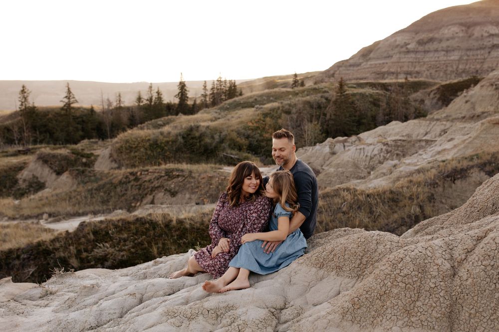 A family enjoys a tender moment together on rugged desert rocks during golden hour.