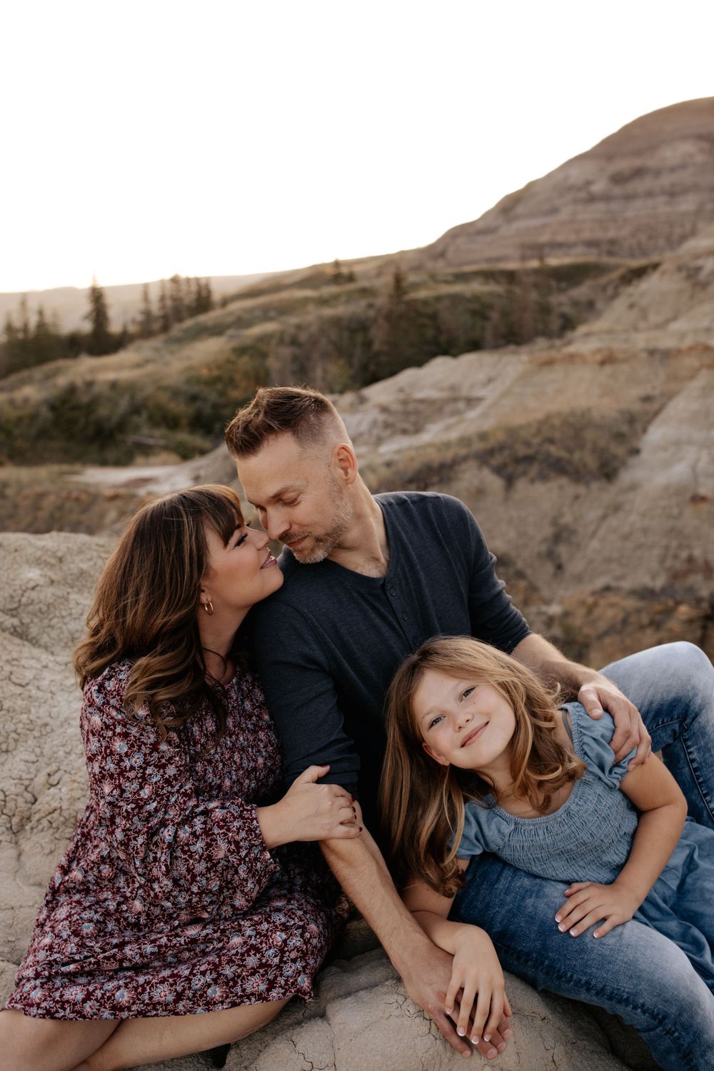 A family cuddles together on rocky terrain during a sunset photoshoot.