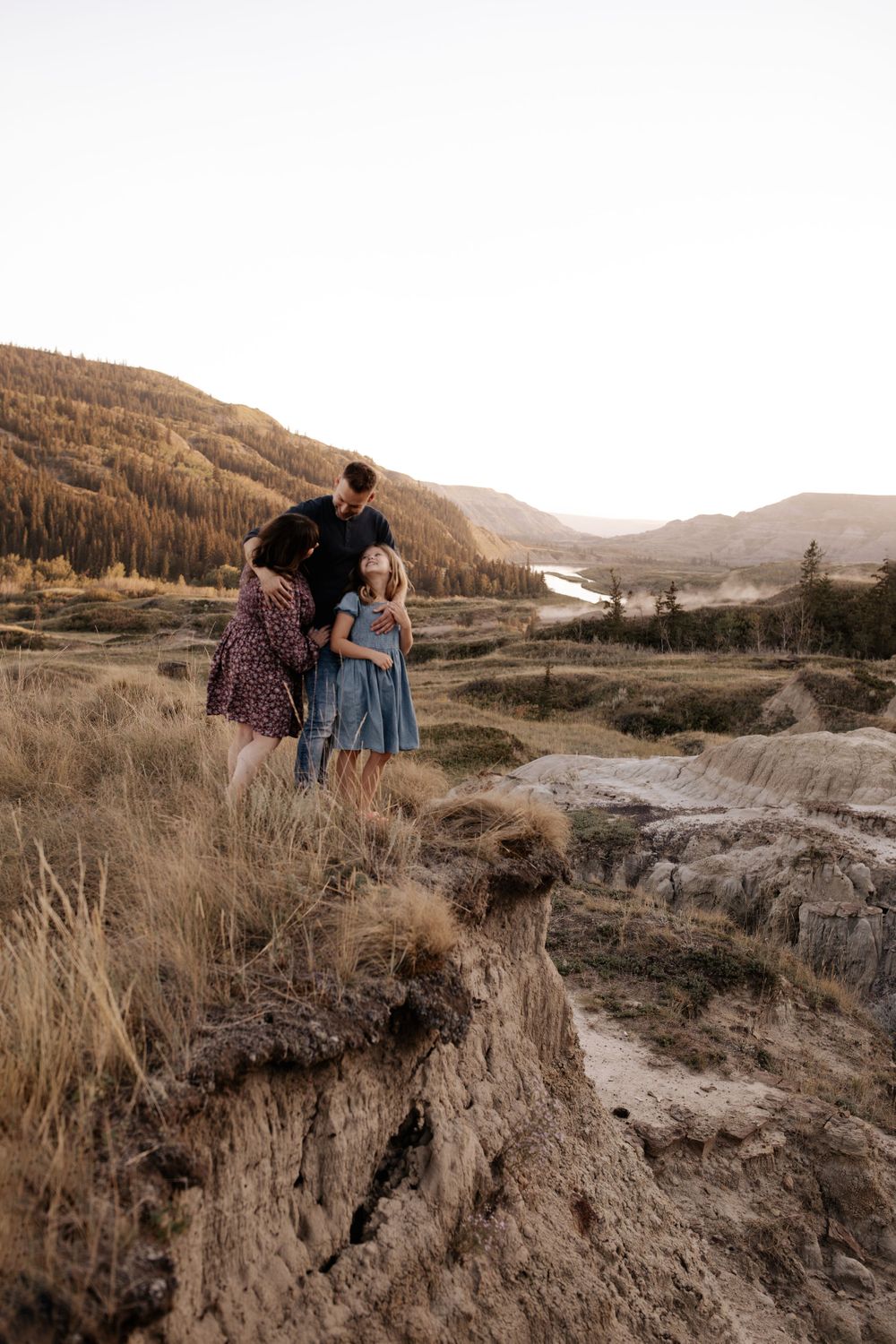 People stand near the edge of a rocky cliff overlooking a vast mountain landscape.