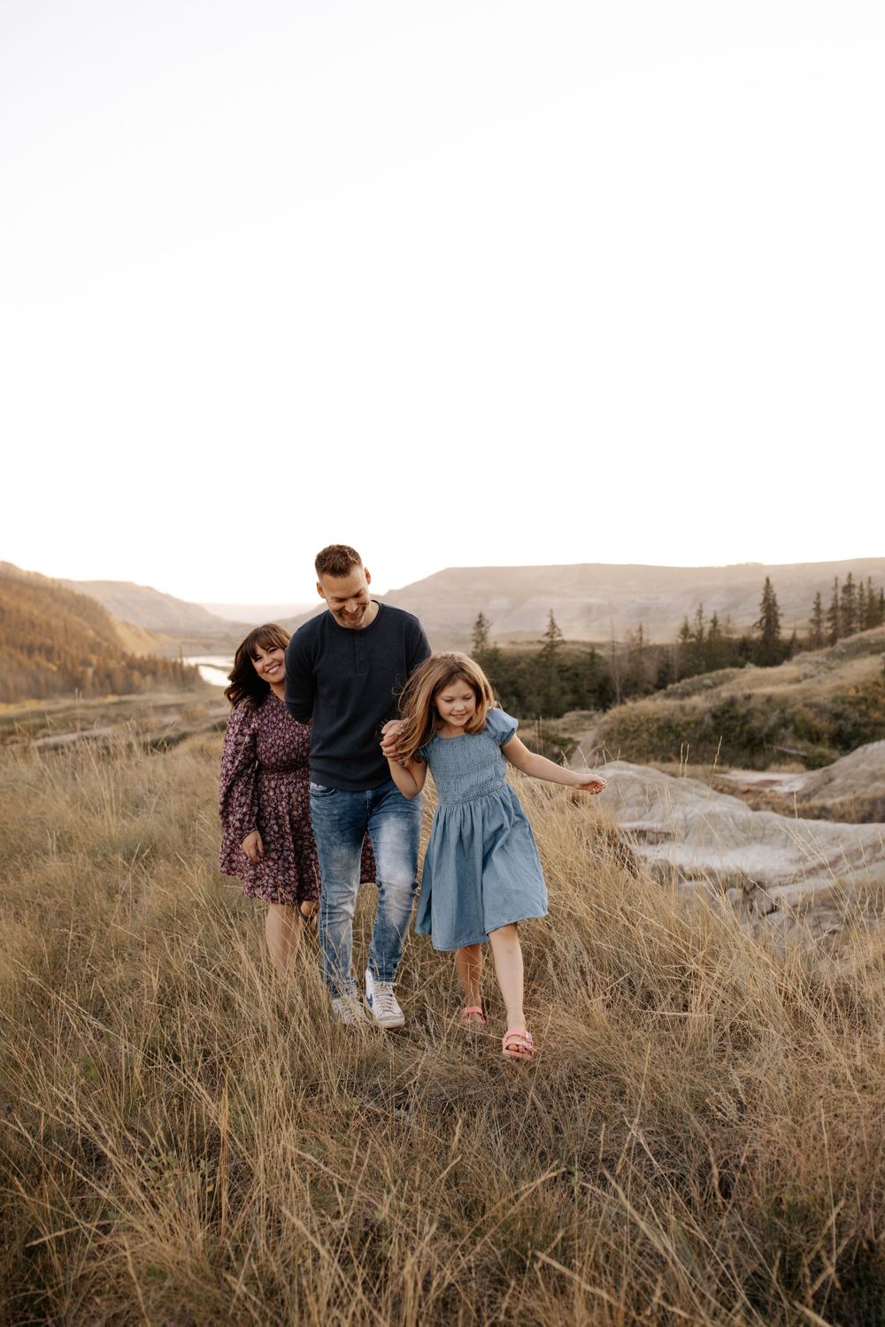 A family enjoying a playful moment together on a grassy hillside during golden hour.