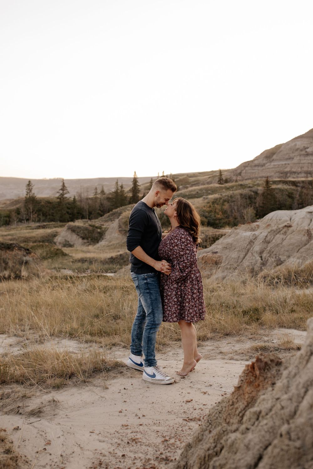 A couple sharing an intimate moment on sandy terrain with mountains in the background.