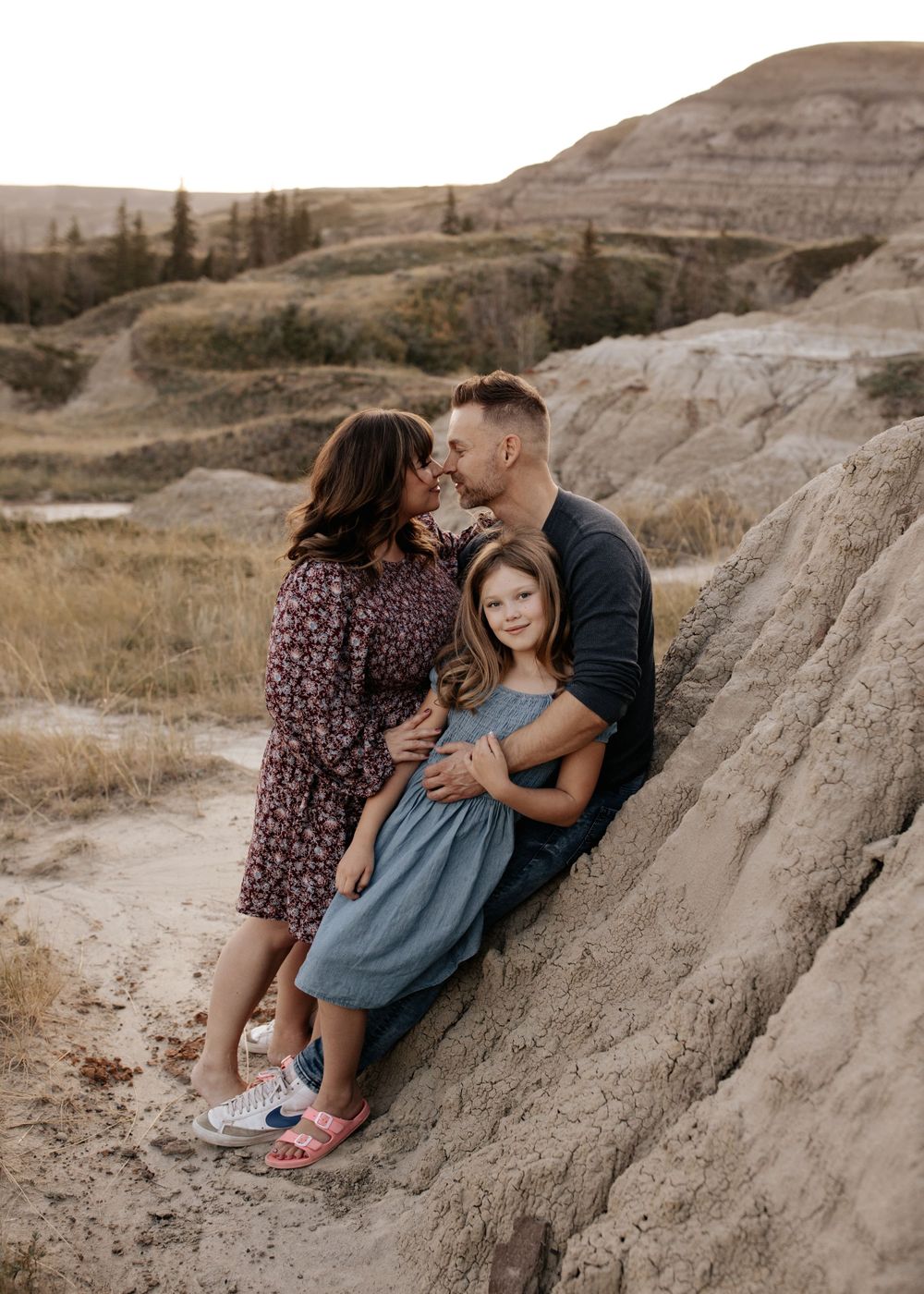 Three people cuddling together on a rocky outcrop in a natural landscape.