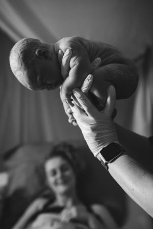 verloskundige houdt baby omhoog voor de apgar check