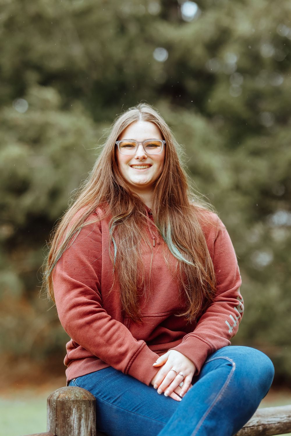 Casual outdoor portrait in coral hoodie and jeans with forest background.