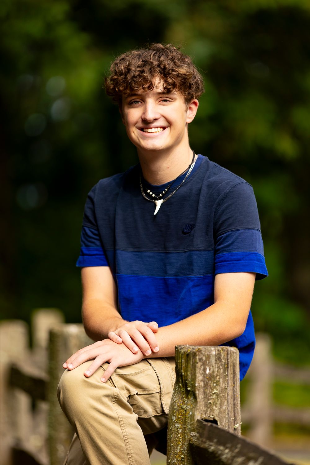 A casual portrait of someone in a navy and blue striped polo shirt sitting on a wooden fence.