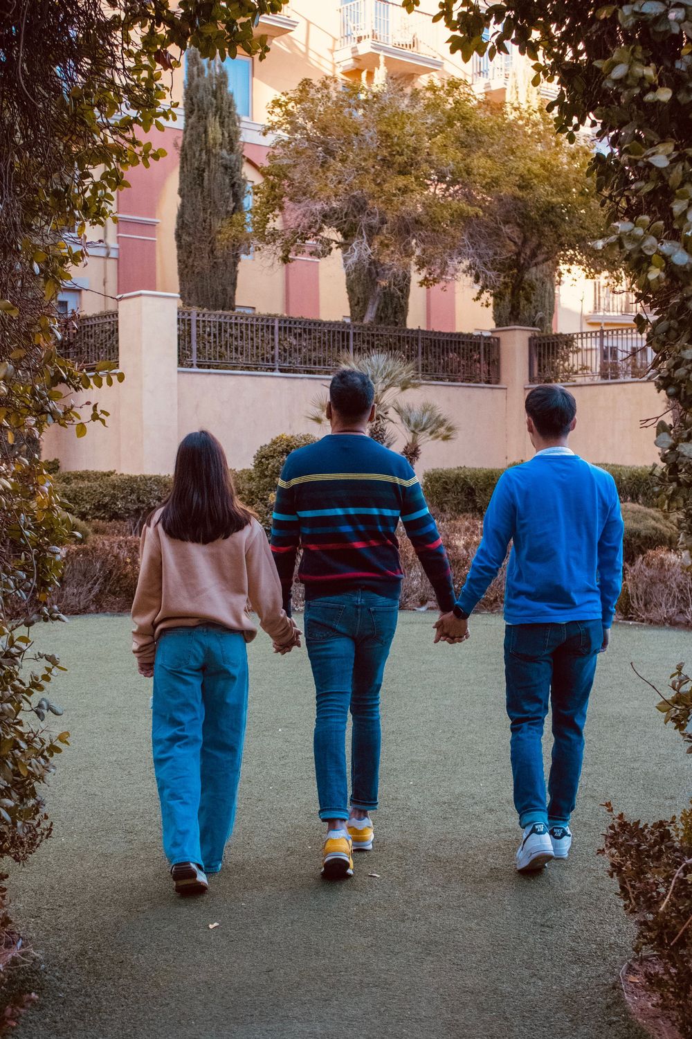 Father and two teenagers walking hand in hand through garden archway at outdoor shopping plaza.