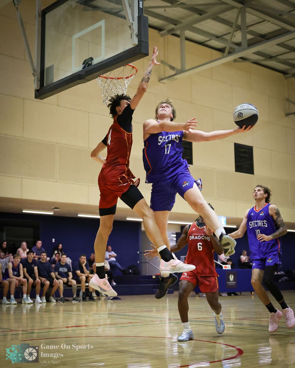 Basketball player in purple Secrets jersey drives to the hoop against a red-uniformed defender during an indoor game.
