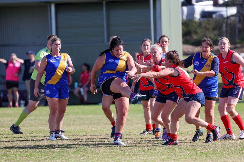 Women's Australian rules football players compete in a match, with players in blue and gold uniforms challenging red and blue opponents.