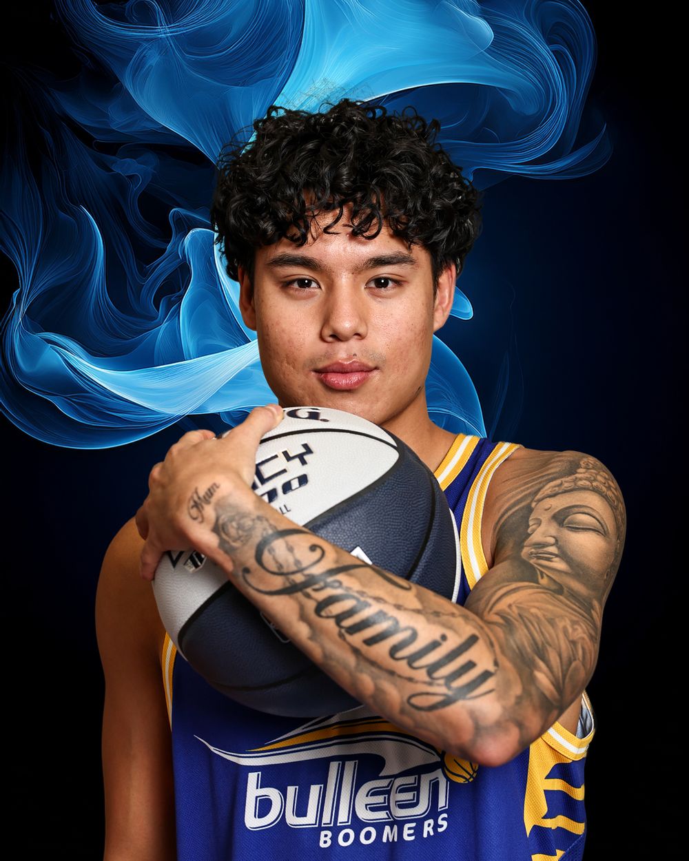 Bulleen Boomers basketball player holding a ball, showing arm tattoos including Family, wearing blue and gold jersey.