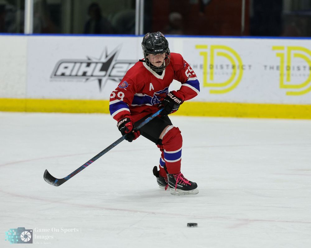 Hockey player in red jersey number 29 skating with puck on indoor ice rink during AIHL game.