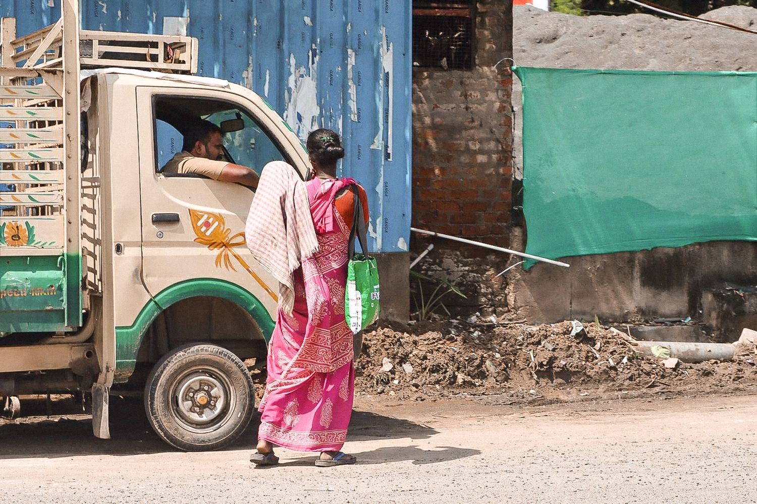 Woman in a pink sari walking past a green van and urban backdrop in South India.