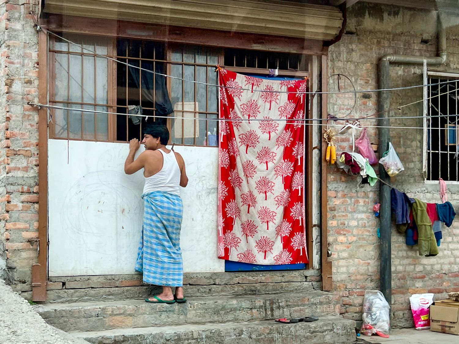 Boy standing barefoot outside a home with a patterned curtain and laundry hanging in Kathmandu, Nepal