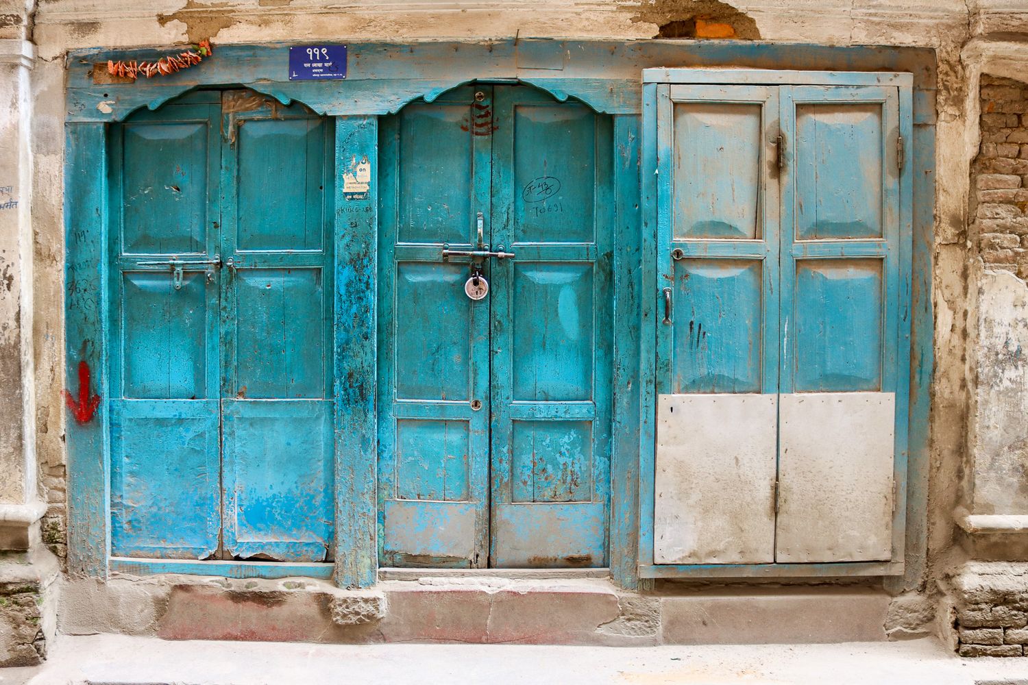 Bright turquoise door with padlock on a worn residential building in Kathmandu, Nepal.