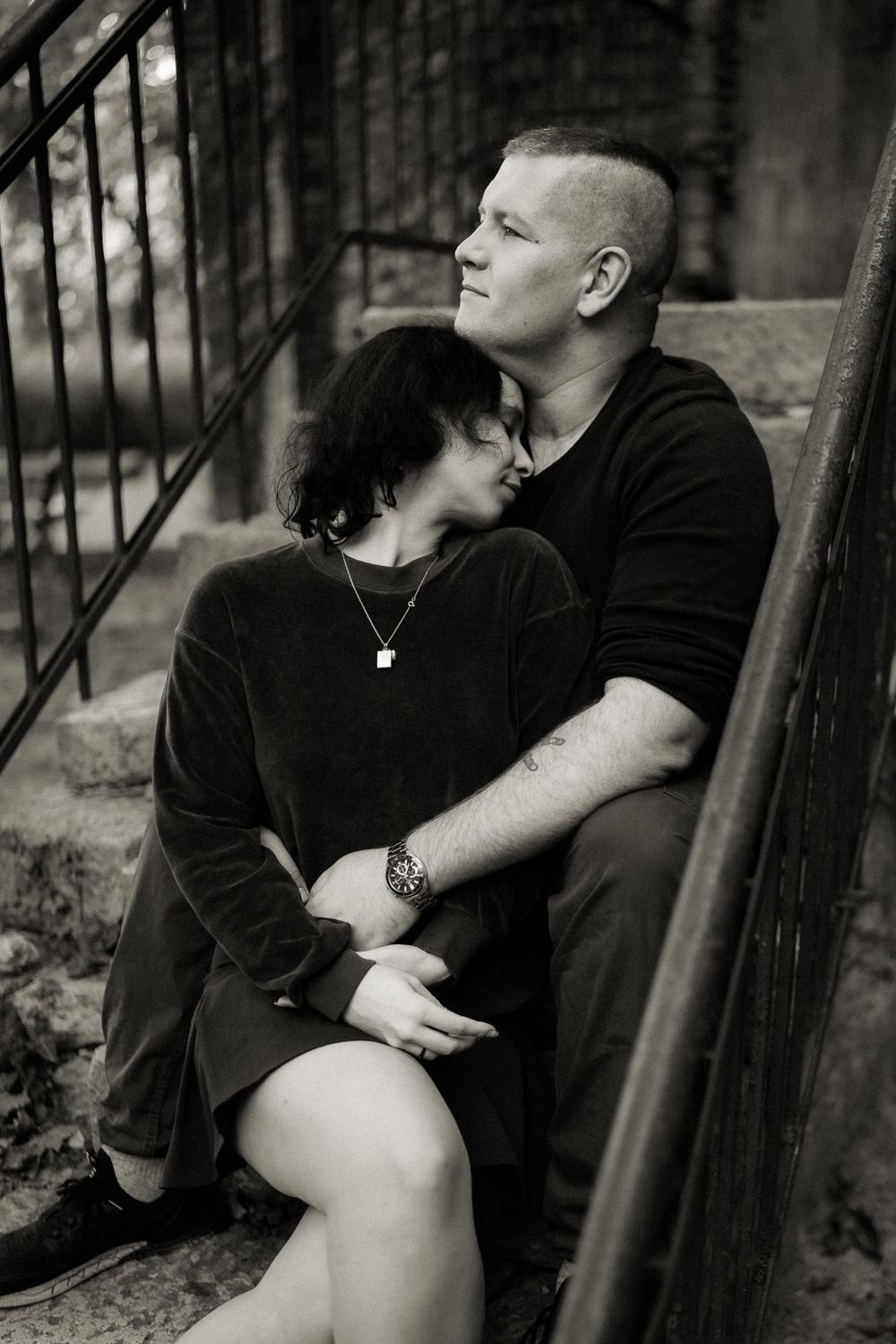Intimate black and white portrait of couple on stone steps with iron railing.