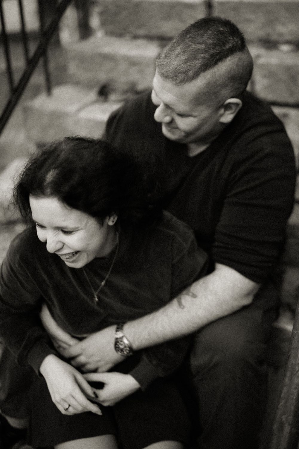 Candid black and white photo showing joyful laughter and embrace on stone steps.