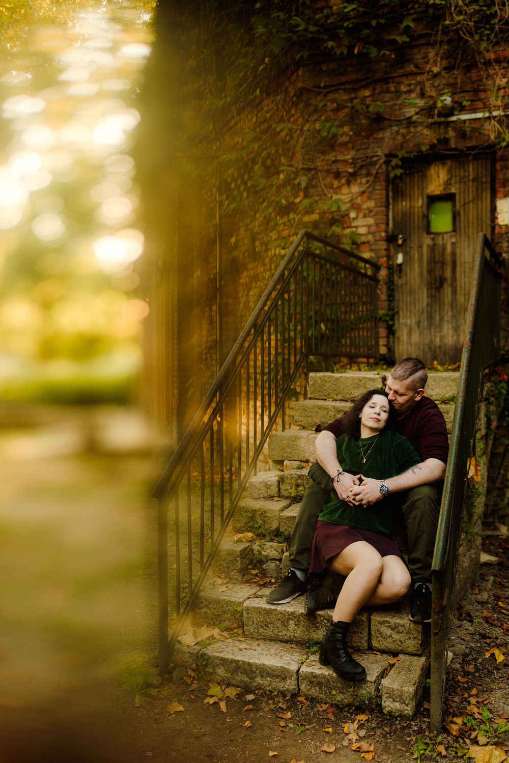Romantic portrait on stone steps with golden sunlight and brick wall backdrop.