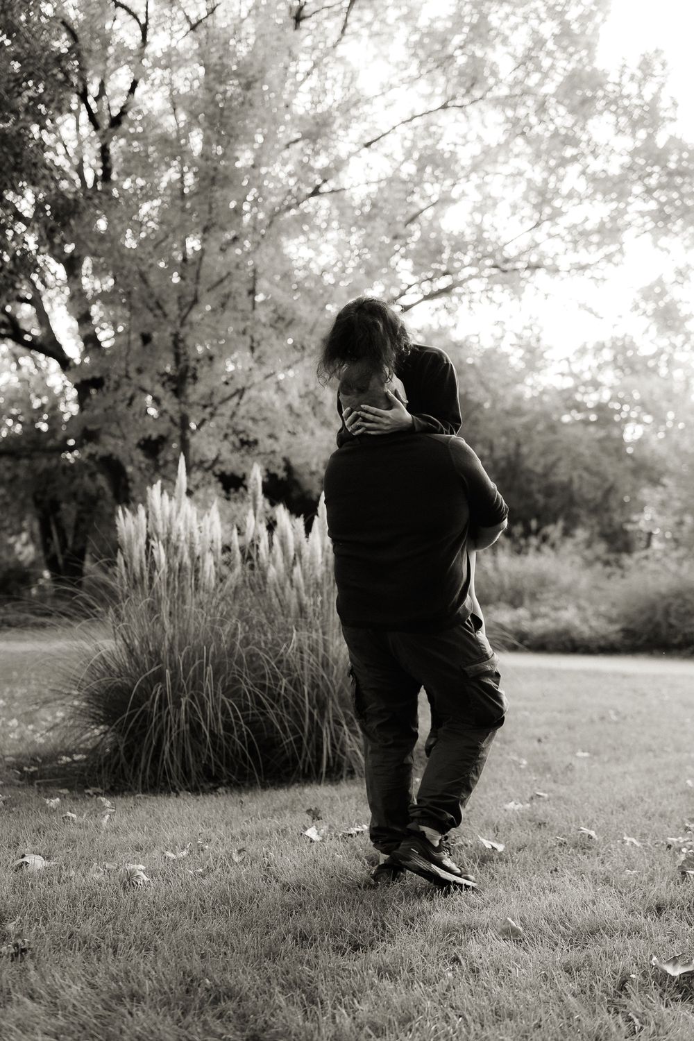 A loving black and white portrait of two people embracing near ornamental grasses.