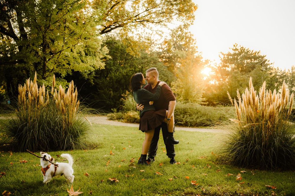 A couple dancing in a garden at sunset with their small white dog watching nearby.