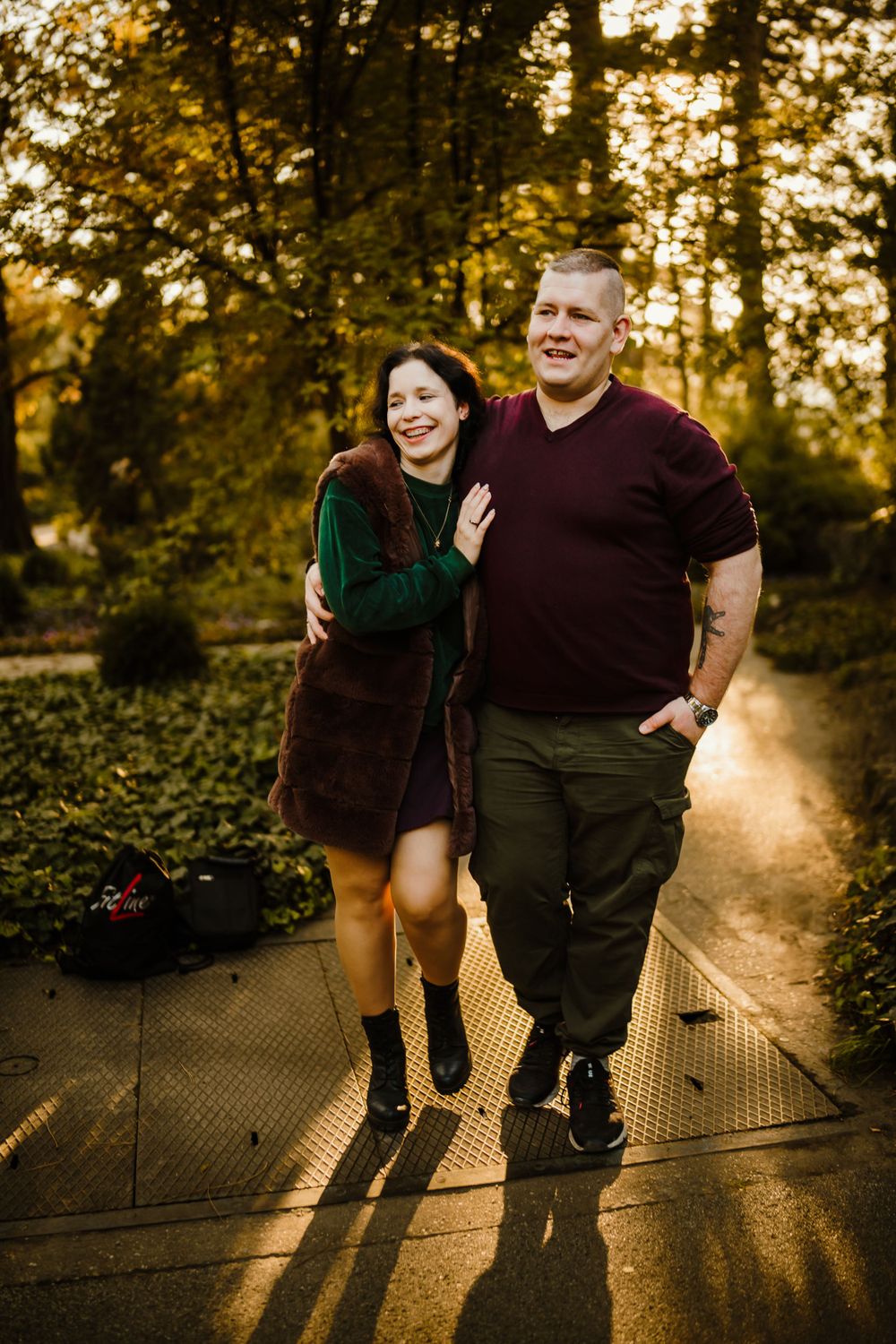A romantic couple laughing together on an autumn path at golden hour in a forest setting.