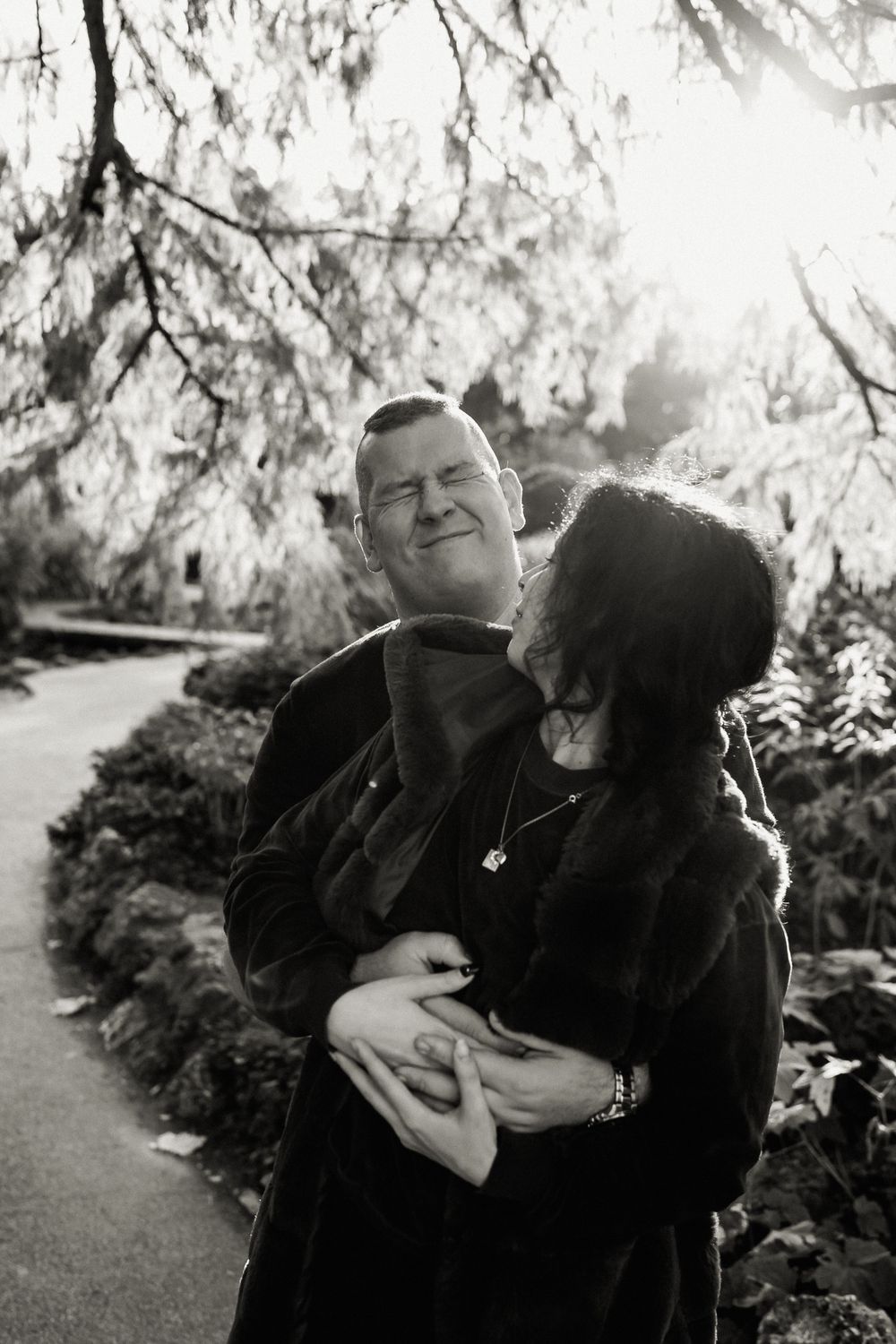 Black and white photograph of a couple sharing a tender moment on a garden path.