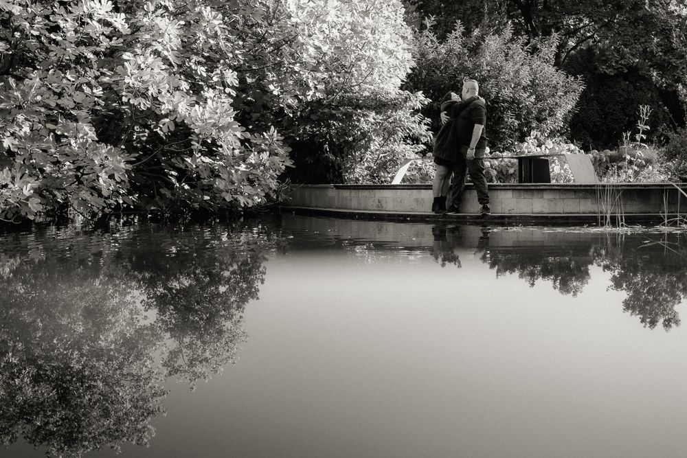 Silhouetted reflection of people standing on a bridge over calm water.