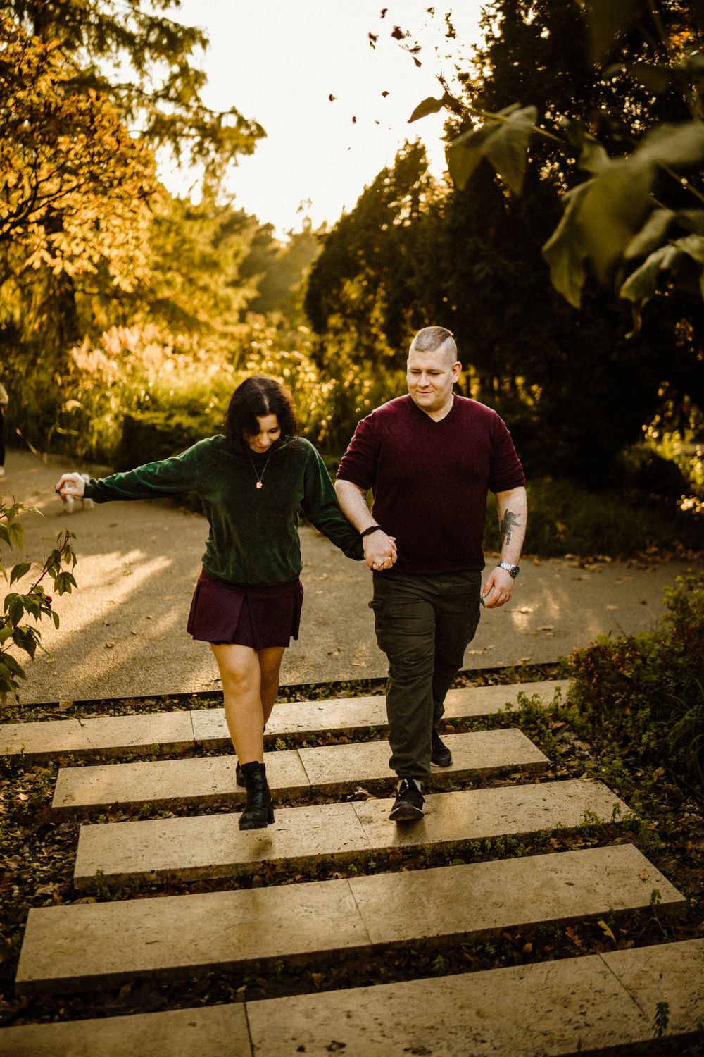 Couple walking down outdoor steps during sunset with autumn leaves falling.