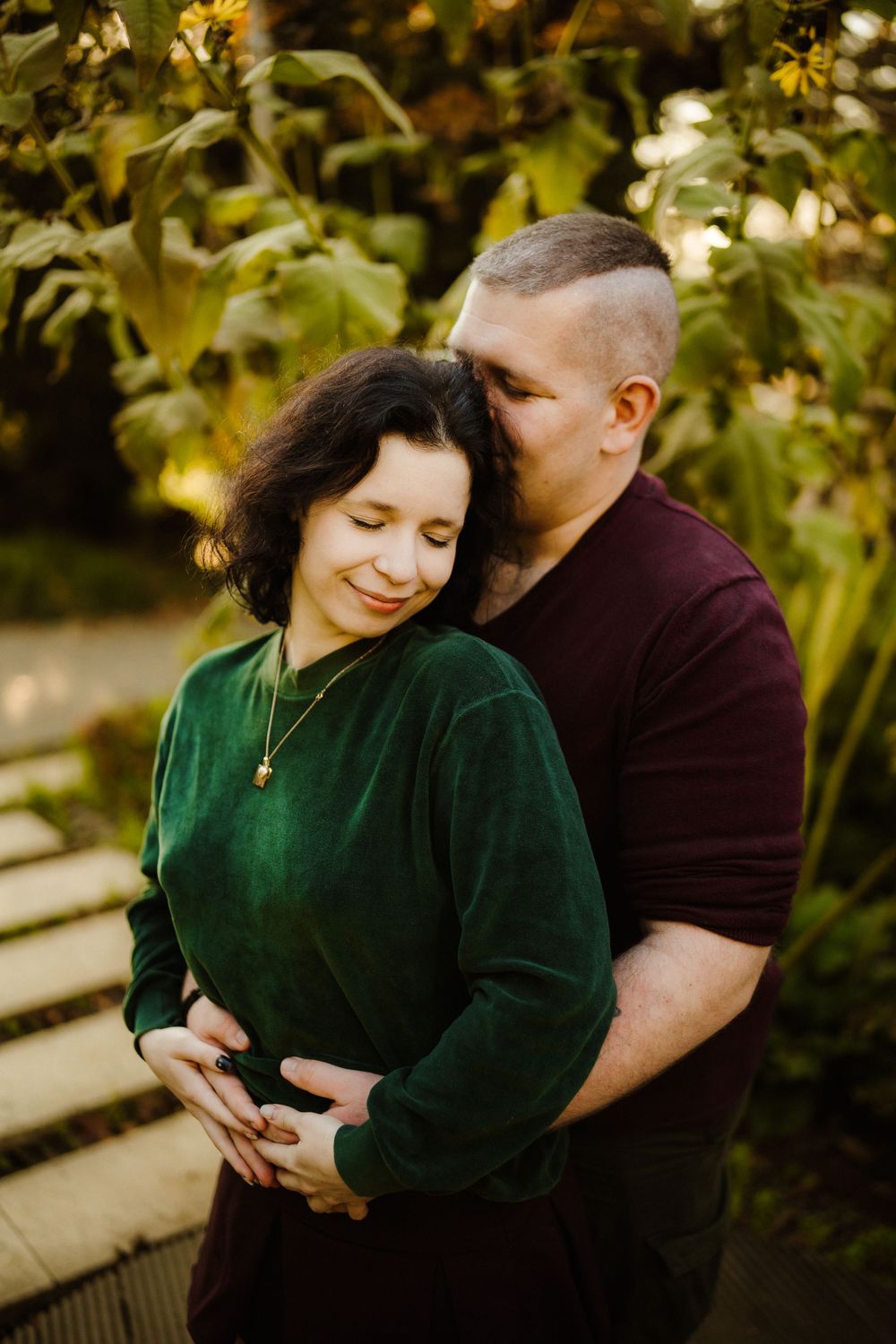 Intimate portrait of a couple embracing in a garden with warm golden lighting.