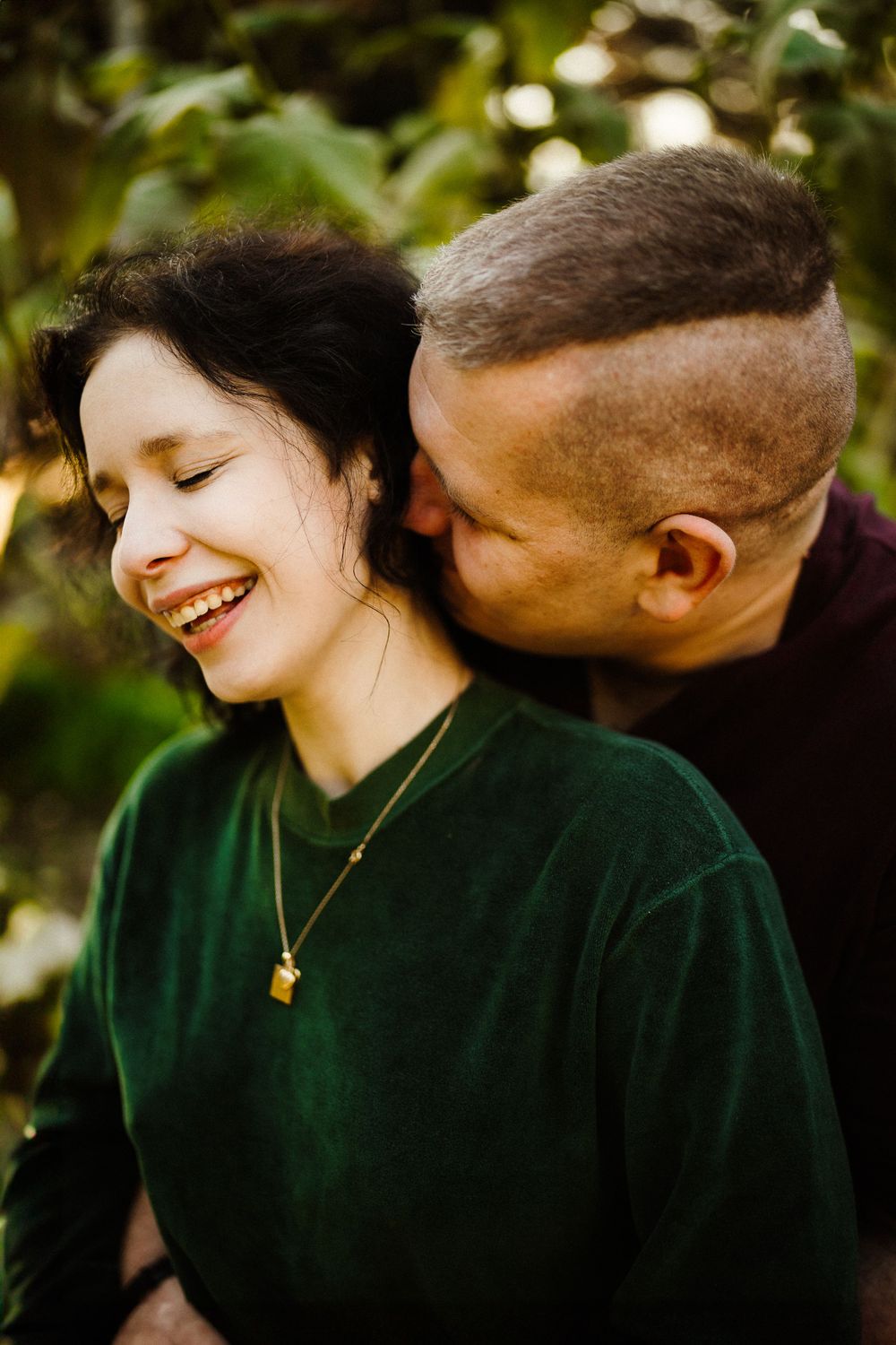 Joyful moment captured between a couple in casual attire against natural foliage.