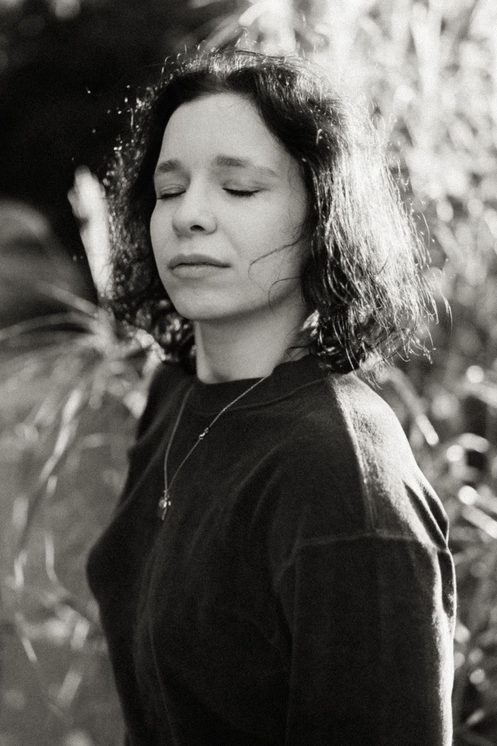 Black and white portrait of a person with eyes closed in serene natural lighting.