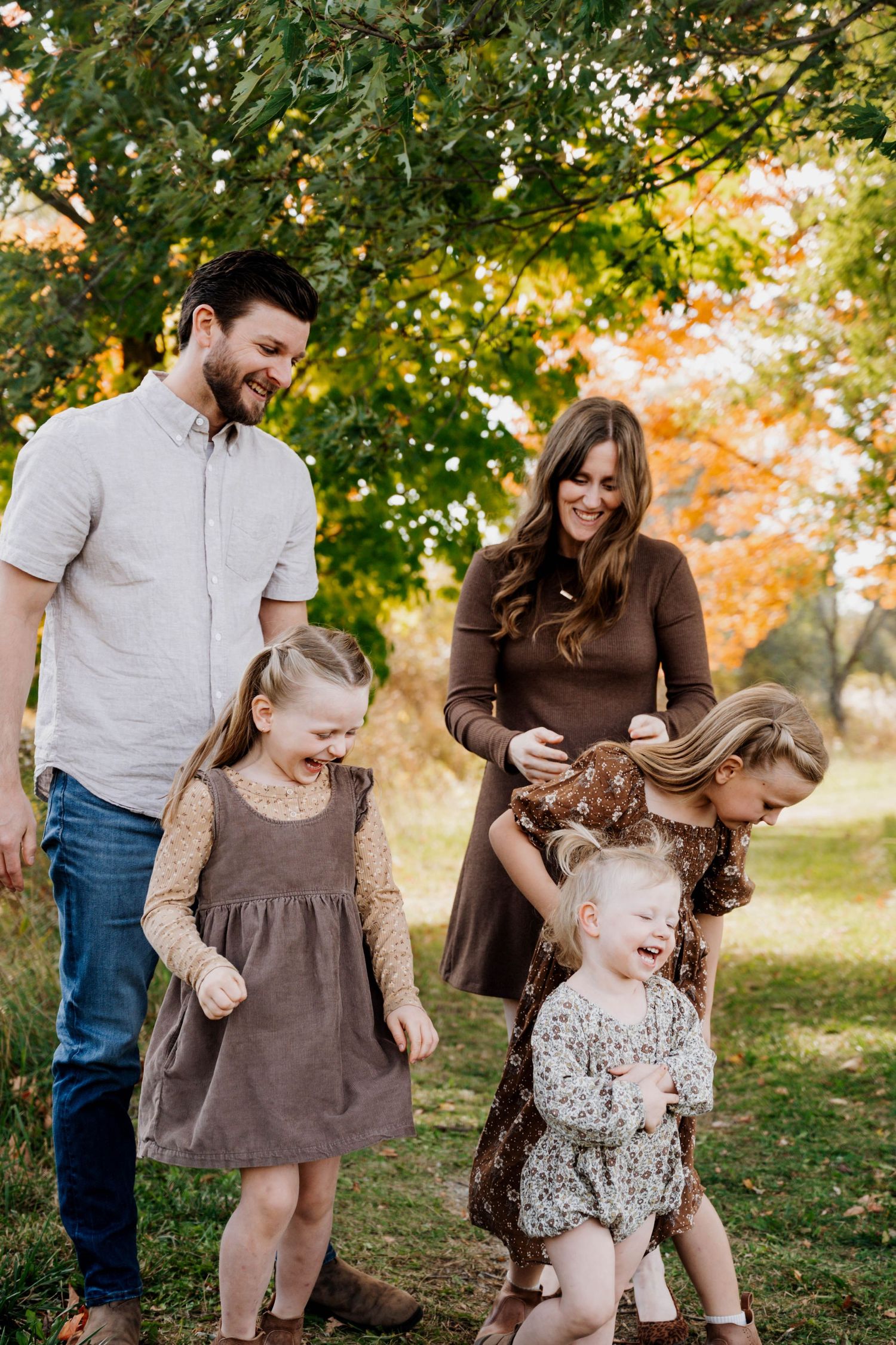 Family shares laughs during autumn photo session in coordinating brown outfits.