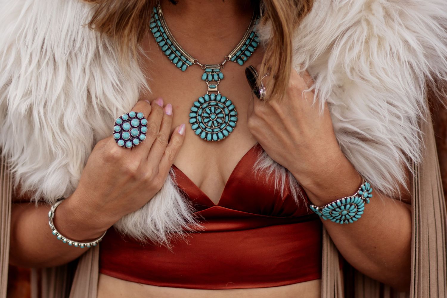 Turquoise statement jewelry and rings styled with white fur coat and red top.