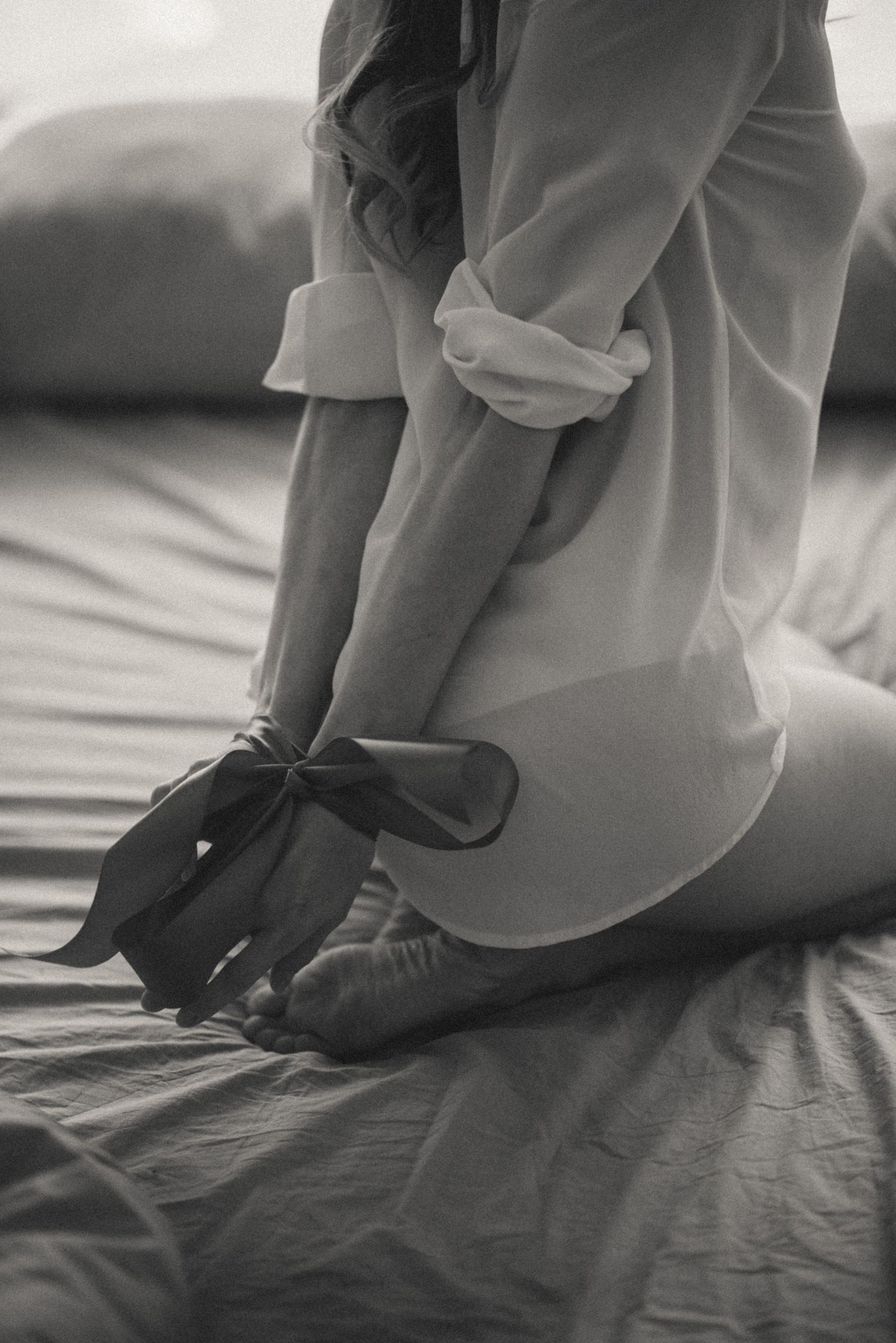 Black and white image of someone sitting on wrinkled bedding.