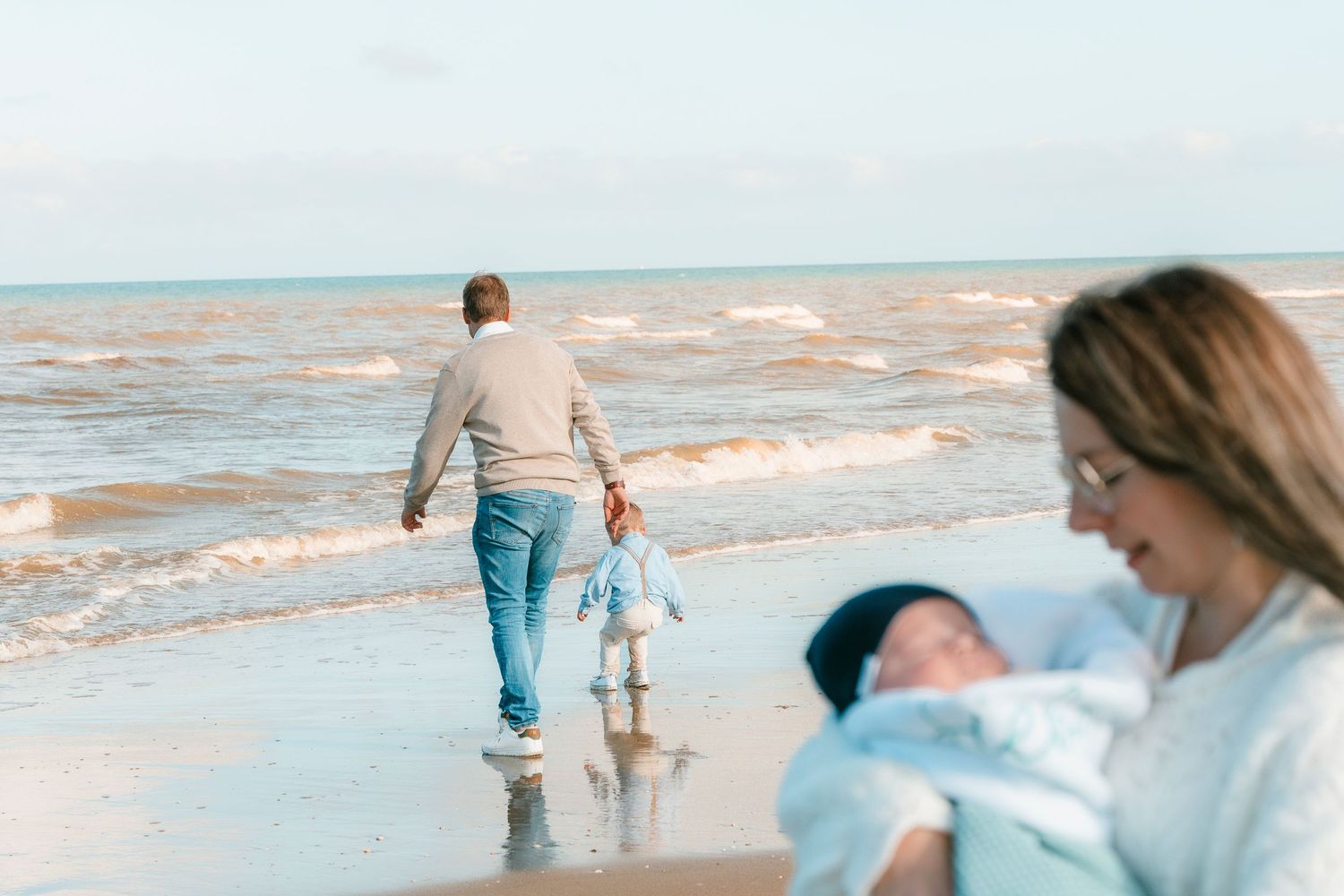 Family spending time together walking along the water's edge at the beach.