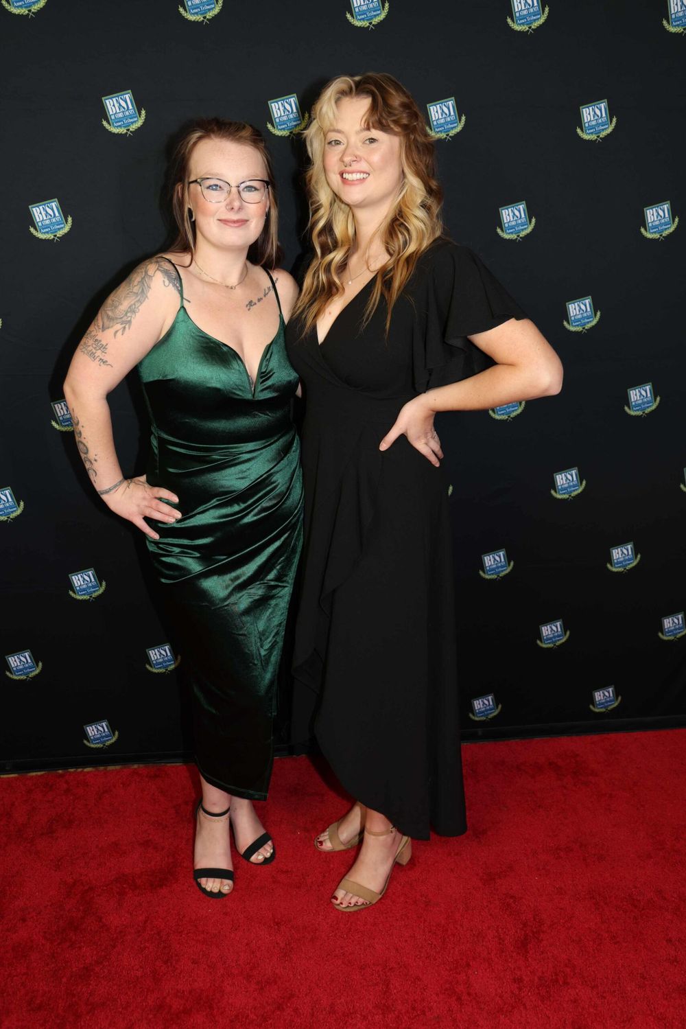 Two people posing on red carpet with branded step-and-repeat backdrop.