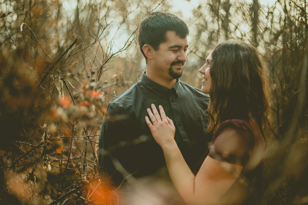 A loving couple shares an intimate moment in a forest during autumn with golden foliage in the background. Edmonton Engagement Photographer