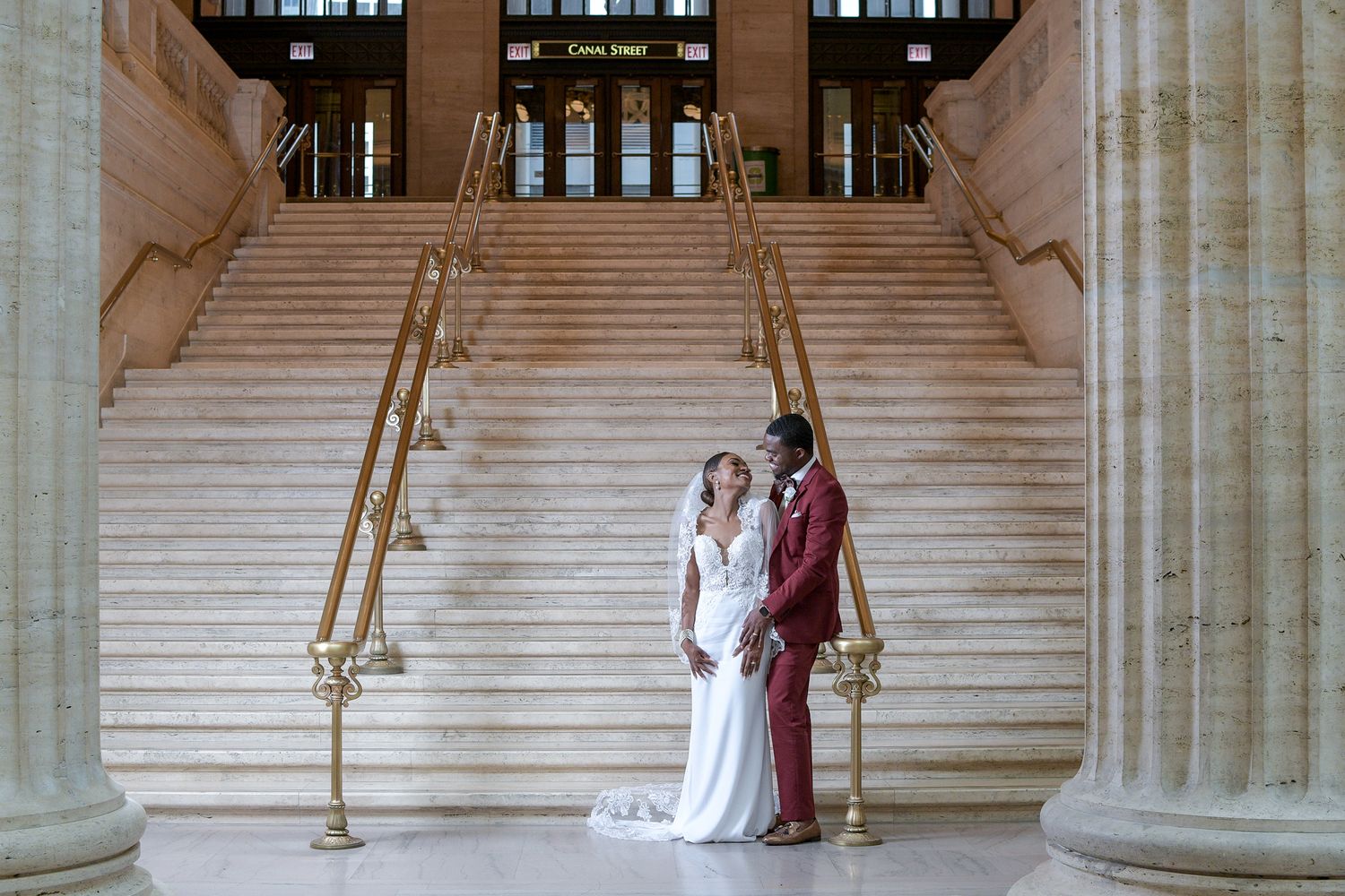 Wedding couple posing on grand marble staircase in classical architecture setting.