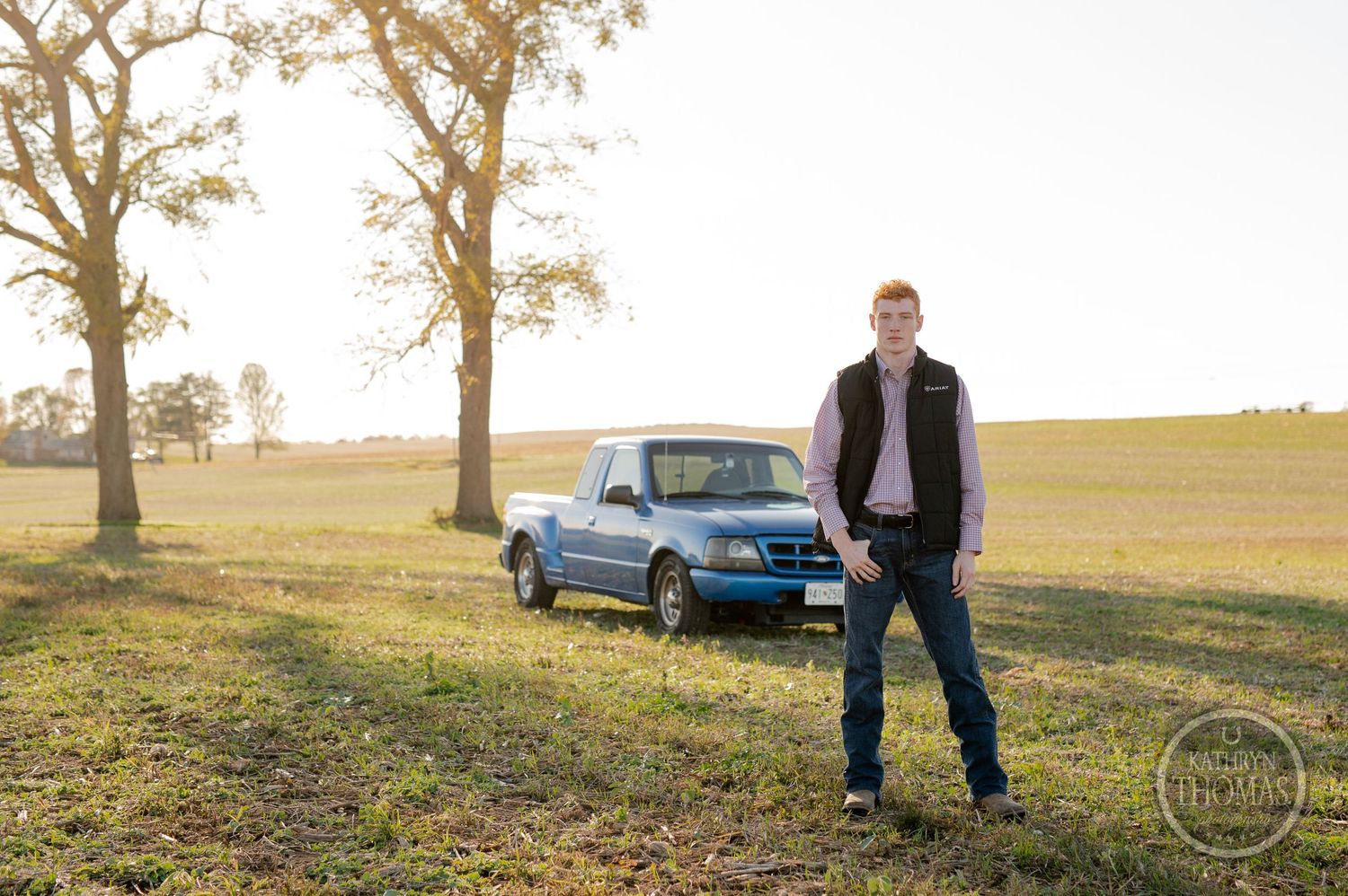 Blue pickup truck parked in a rural field with trees at sunset.