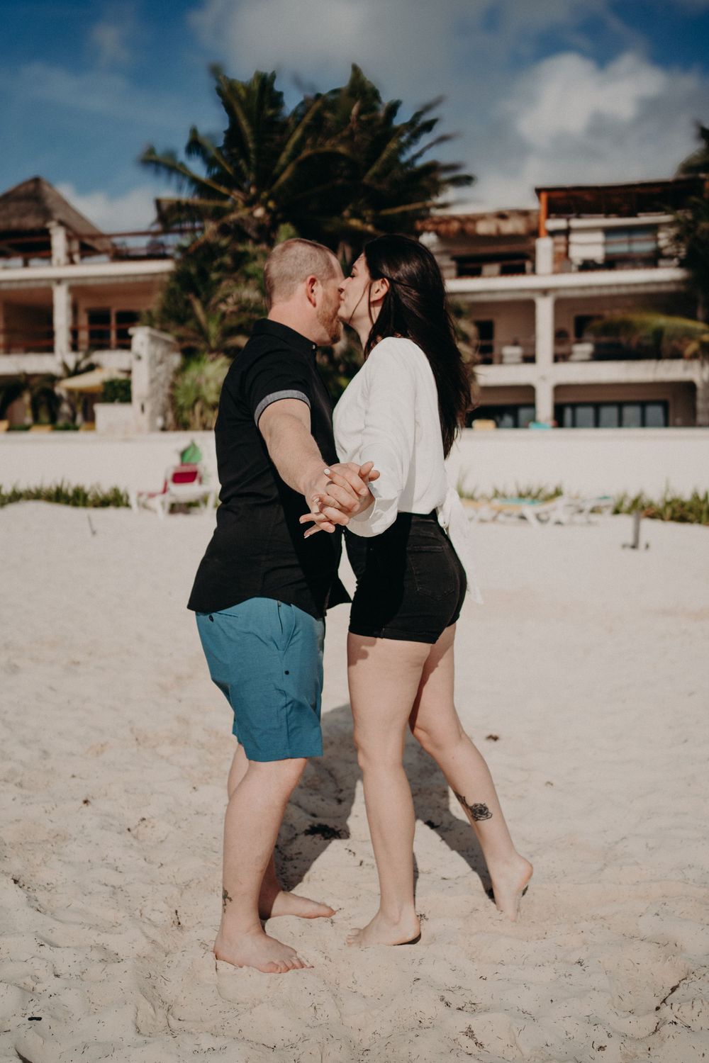 A romantic beachside scene with tropical resort buildings and palm trees in the background photoshoot in Puerto Morelos.