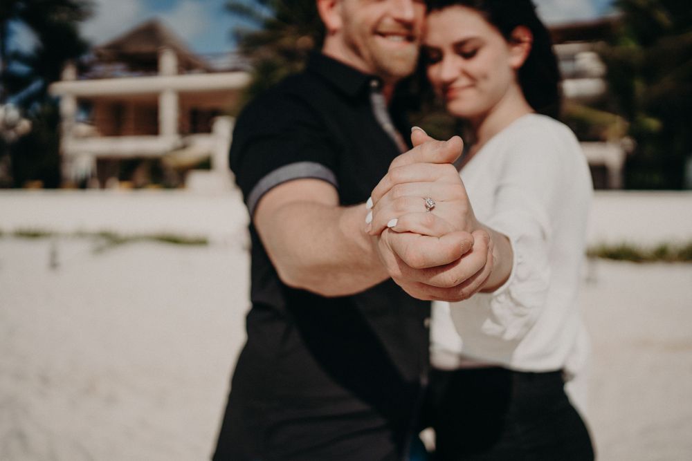A joyful moment shared on a sandy beach with resort buildings visible in the background photoshoot in Puerto Morelos.