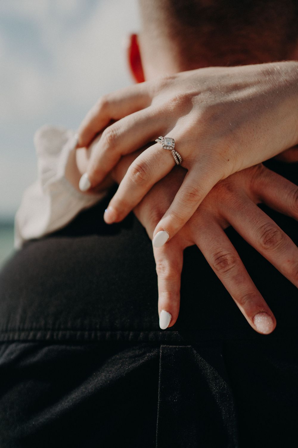 Delicate hand with white manicure and engagement ring resting against dark fabric photoshoot in Puerto Morelos.