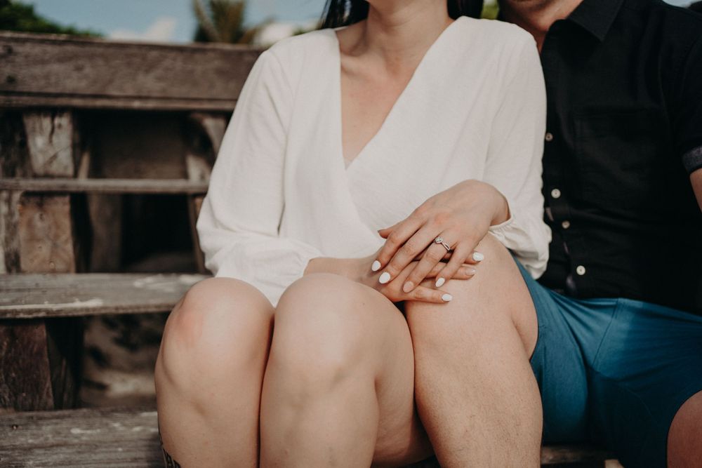 A couple sitting close together on wooden steps with hands clasped, wearing white and dark clothing photoshoot in Puerto Morelos.