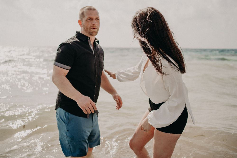 A playful couple enjoying time together at the beach with waves in the background photoshoot in Puerto Morelos.