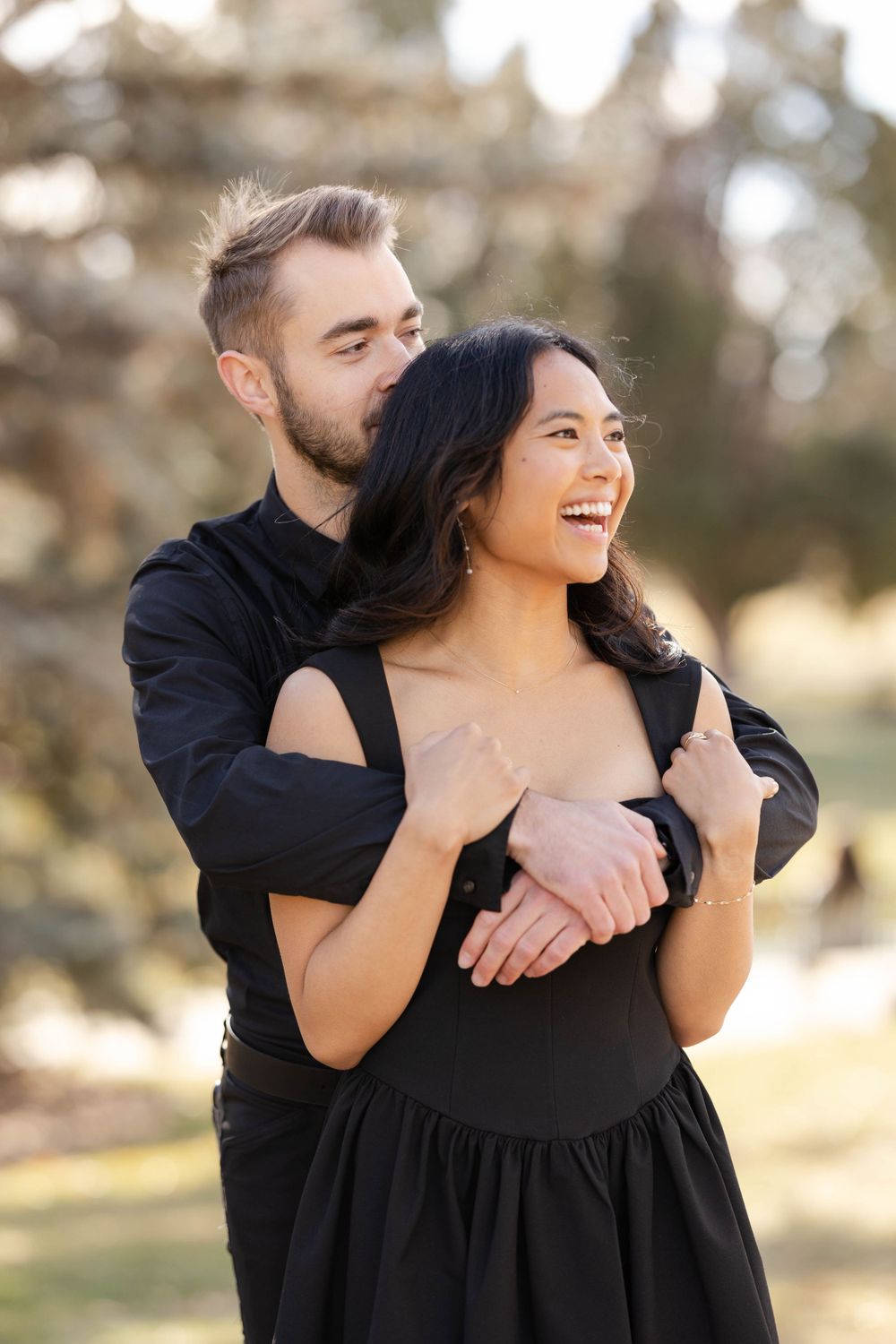 Couple shares joyful embrace during outdoor portrait session in natural setting.