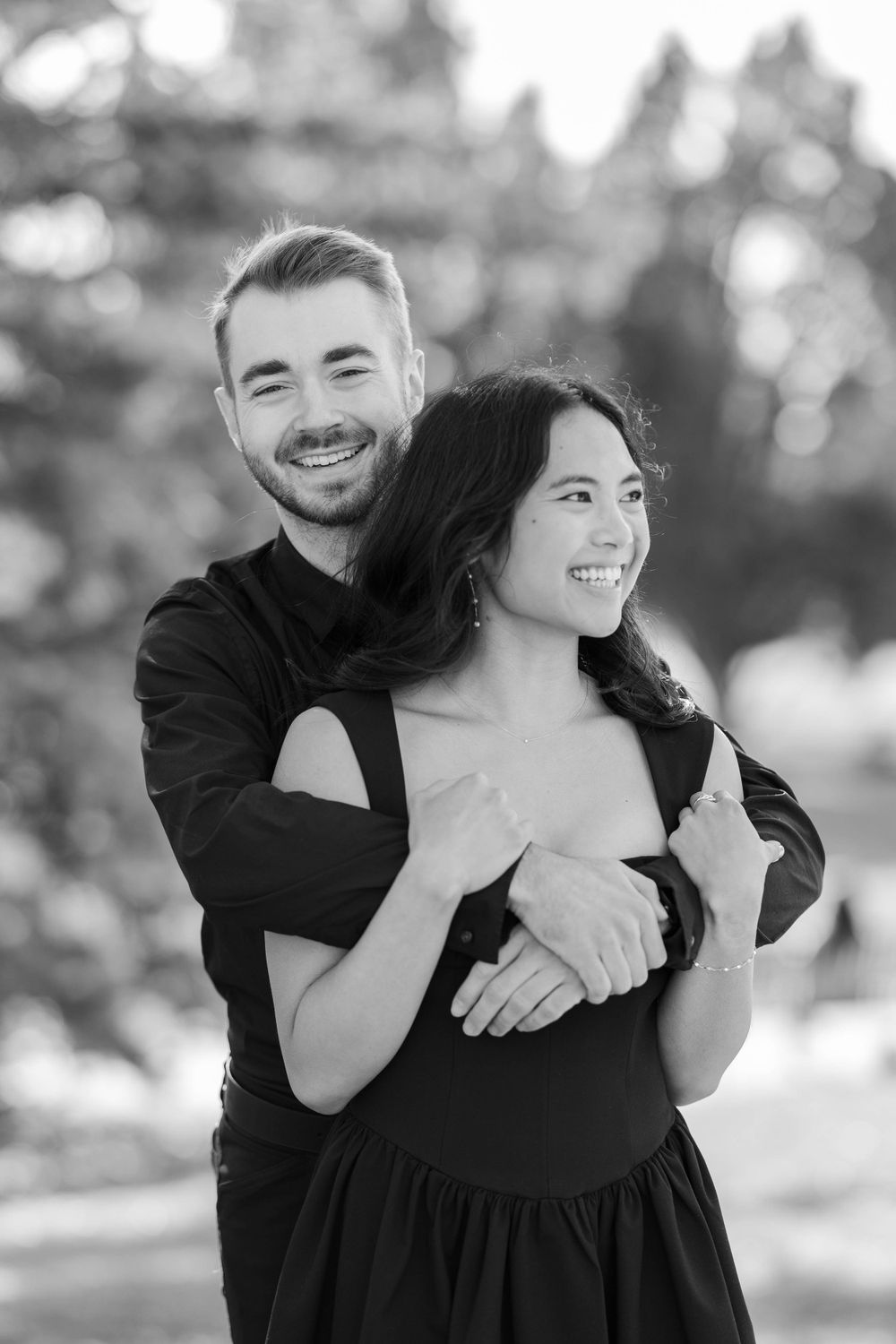A black and white romantic couple portrait with gentle embrace outdoors with soft bokeh background.