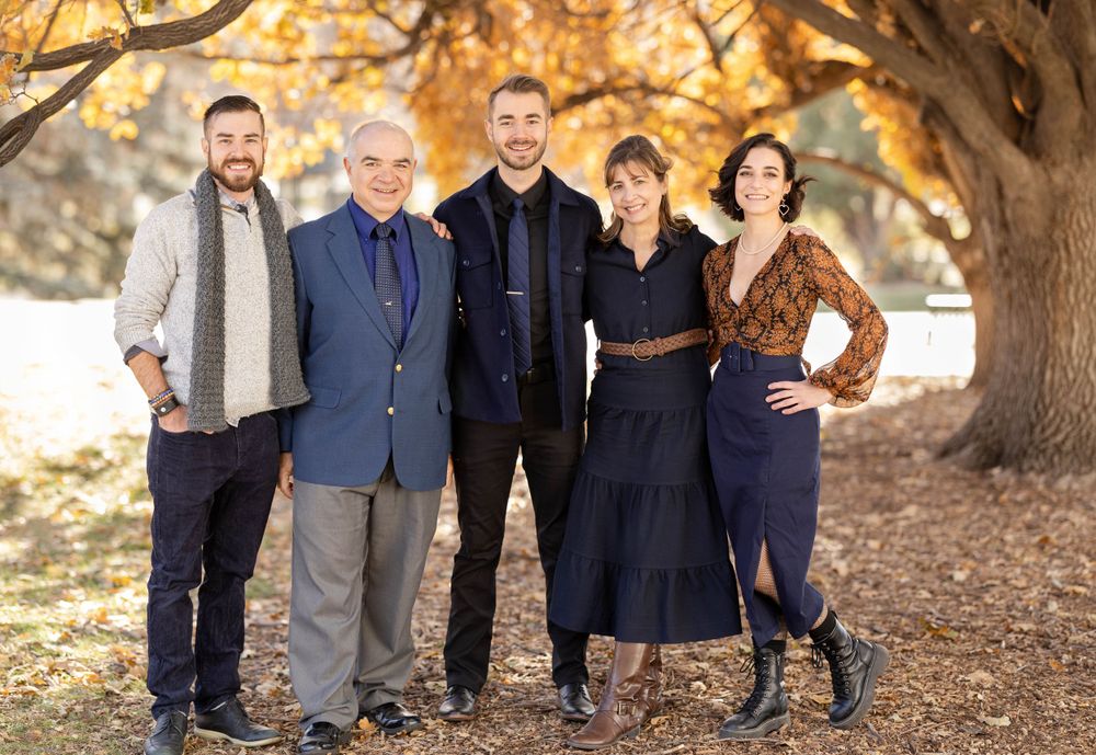 Family portrait with five people under autumn trees wearing coordinated outfits.