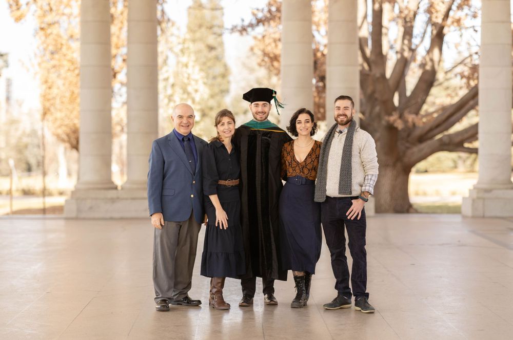 Graduation photo with family members and graduate in academic regalia under classical columns.